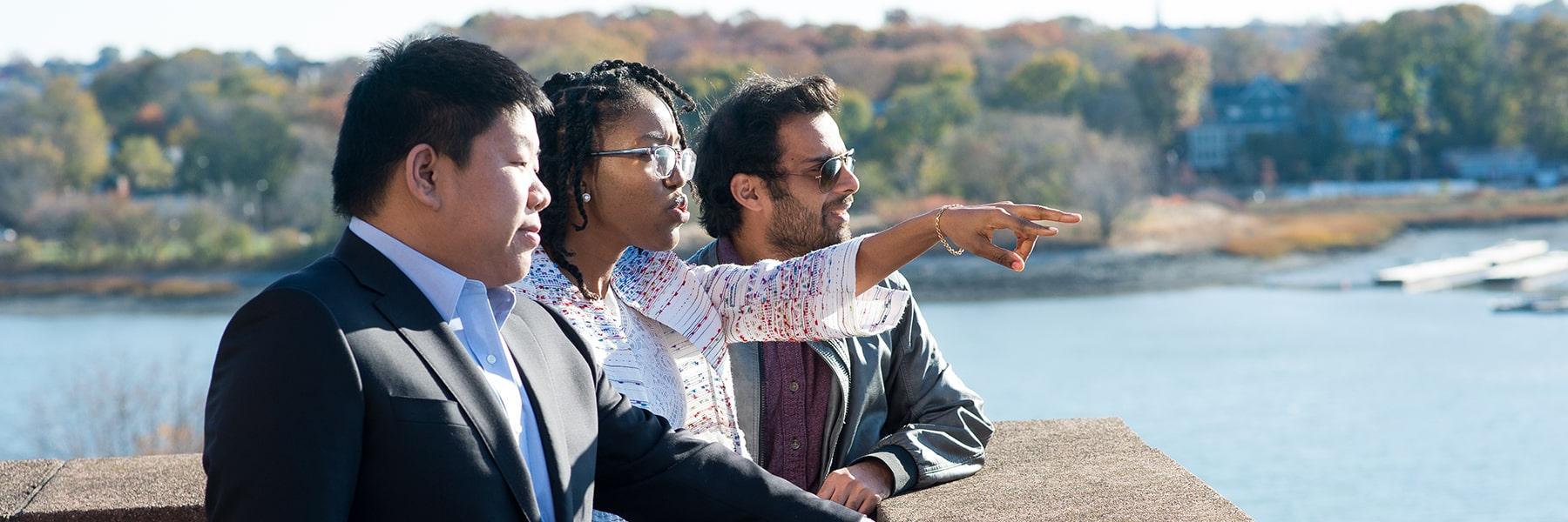 Three graduate students look over Savin Hill cover from terrace on campus.